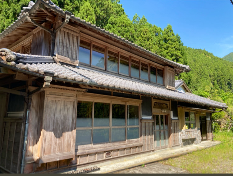 青い空に緑の山が映える景観の中に佇む古民家宿の外観