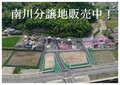 南川分譲地販売中! 後方に木々があり、整備された道路と住宅が並んでいる場所にある分譲地を上空から写した写真