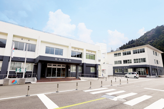 横断歩道のある道路の奥に、入り口部分の庇と1階部分が黒、2階と3階部分が白の外壁をした那賀町役場が建っている写真
