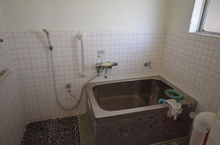 床と壁の下半分がタイル張りで、銀色の浴槽が設置されている浴室の写真