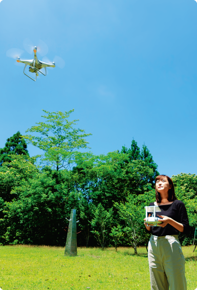 青空のもと、芝生が広がる屋外でドローンを飛ばしている女性の写真