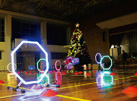 奥にクリスマスツリーがあり、その周囲に設置されたドローンがくぐる障害物がカラフルに光っている写真