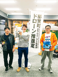 「那賀町ドローン推進室」と書かれたのぼり旗と喜多幸治さん(写真右)、 渡邊槙太郎さん(写真中)、有田光一郎さん(写真左)の写真