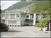 後方に山が見え、垂れ幕が掲げられている2階建ての校舎を校門付近から撮影した那賀高校の外観写真