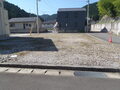 青空の下左手に住宅があり、右手の山に面している道路にコの字に囲まれた区画2南川312-15の写真