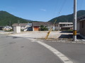 背景に青い空と山々が映り、住宅が奥と右手側にある道路に面した区画3南川312の写真
