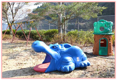 緑豊かな自然を背景に、公園にある青いカバの置物と遊具の写真