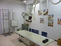 天井から吊り下げられたレントゲンの装置と中央に置かれたベットがあるレントゲン室内の写真