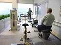 トレーニングバイクなどの器具が置かれ、年配の男性がトレーニングをしている筋トレコーナーの写真