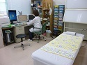 左側の机はモニターが3台置かれ、席に座ってパソコンで作業をしている白衣の女性、レントゲンを写すシャウカステン、左側にはベットが置かれている診察室の様子の写真