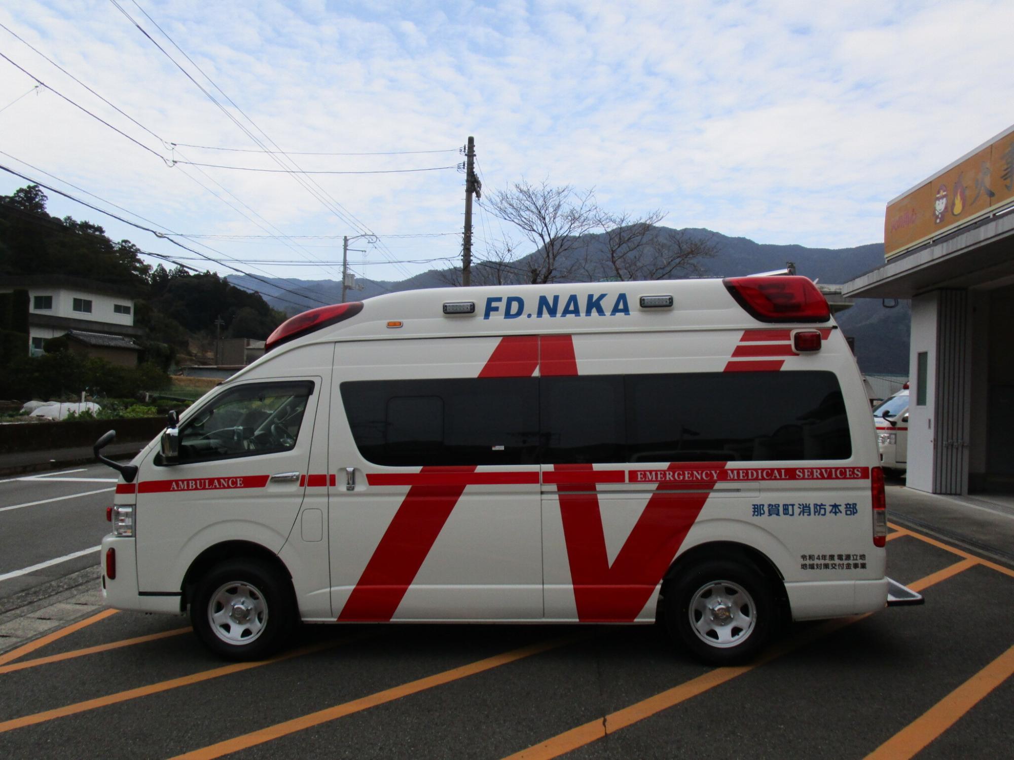 車両のルーフ部分に赤色のワイドランプを持ち、白いボディに赤いラインと那賀町消防本部と書かれた救急車を左側から写した写真