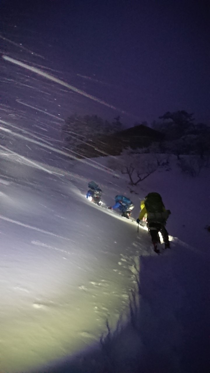 暗くなった山道を、ライトで照らしながら登山をしている数名の隊員の写真