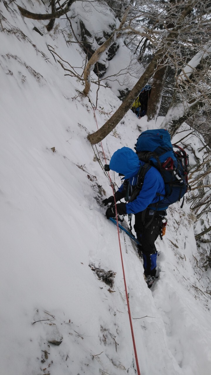 雪の積もった急斜面を、ロープを使いながら登山をしている隊員の写真
