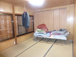 奥にクローゼットが設置され、パイプベットの上に布団や敷物が置かれた和室の写真