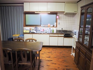 奥に流し台とコンロ、右側に食器棚、手前に4人掛けのテーブルと椅子が設置されているキッチンの写真