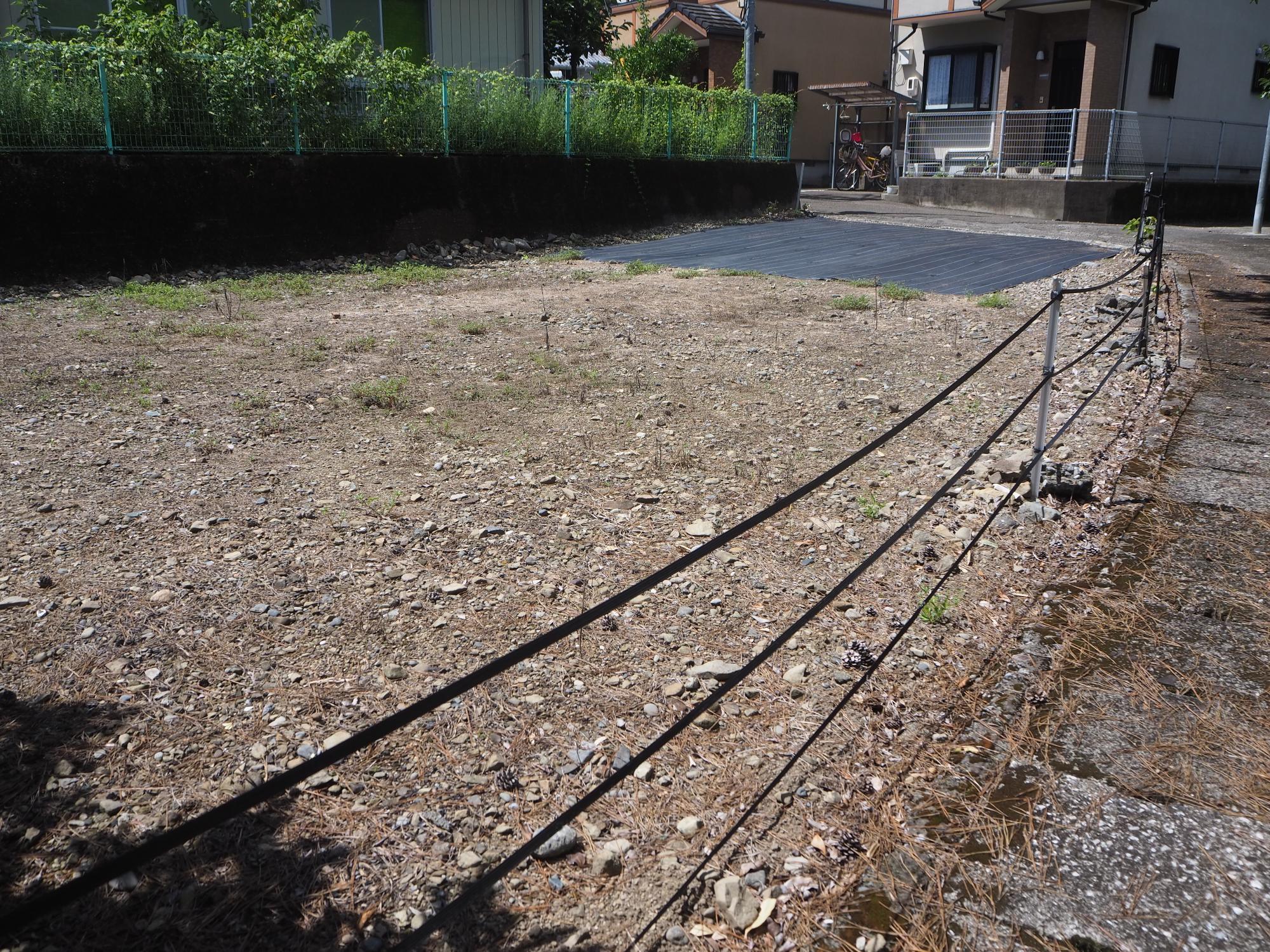 土地の境をロープで区切り奥には民家が見える空き土地の写真