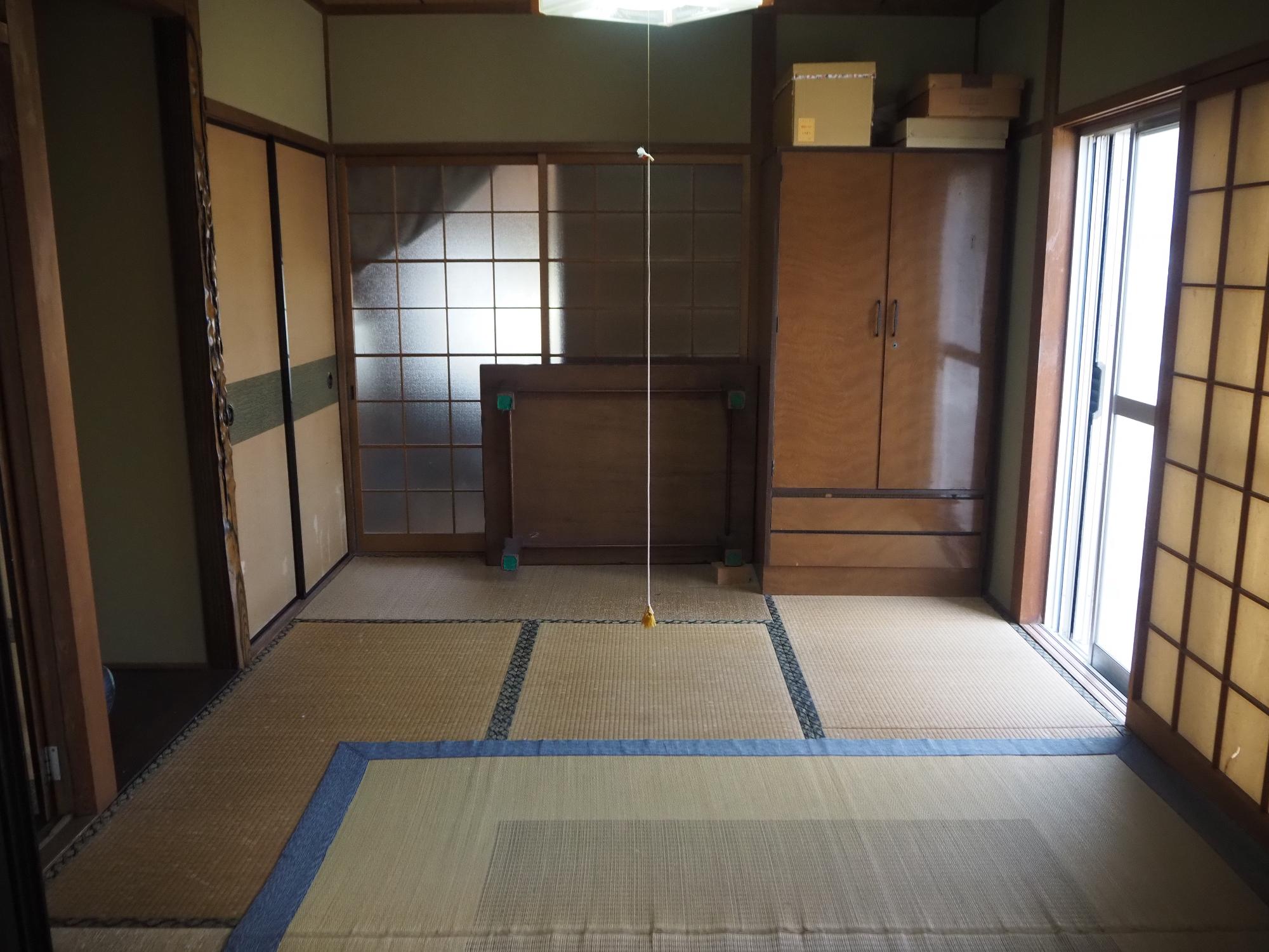 奥に引き戸とタンスが有り真ん中に電気の線が垂れている和室
