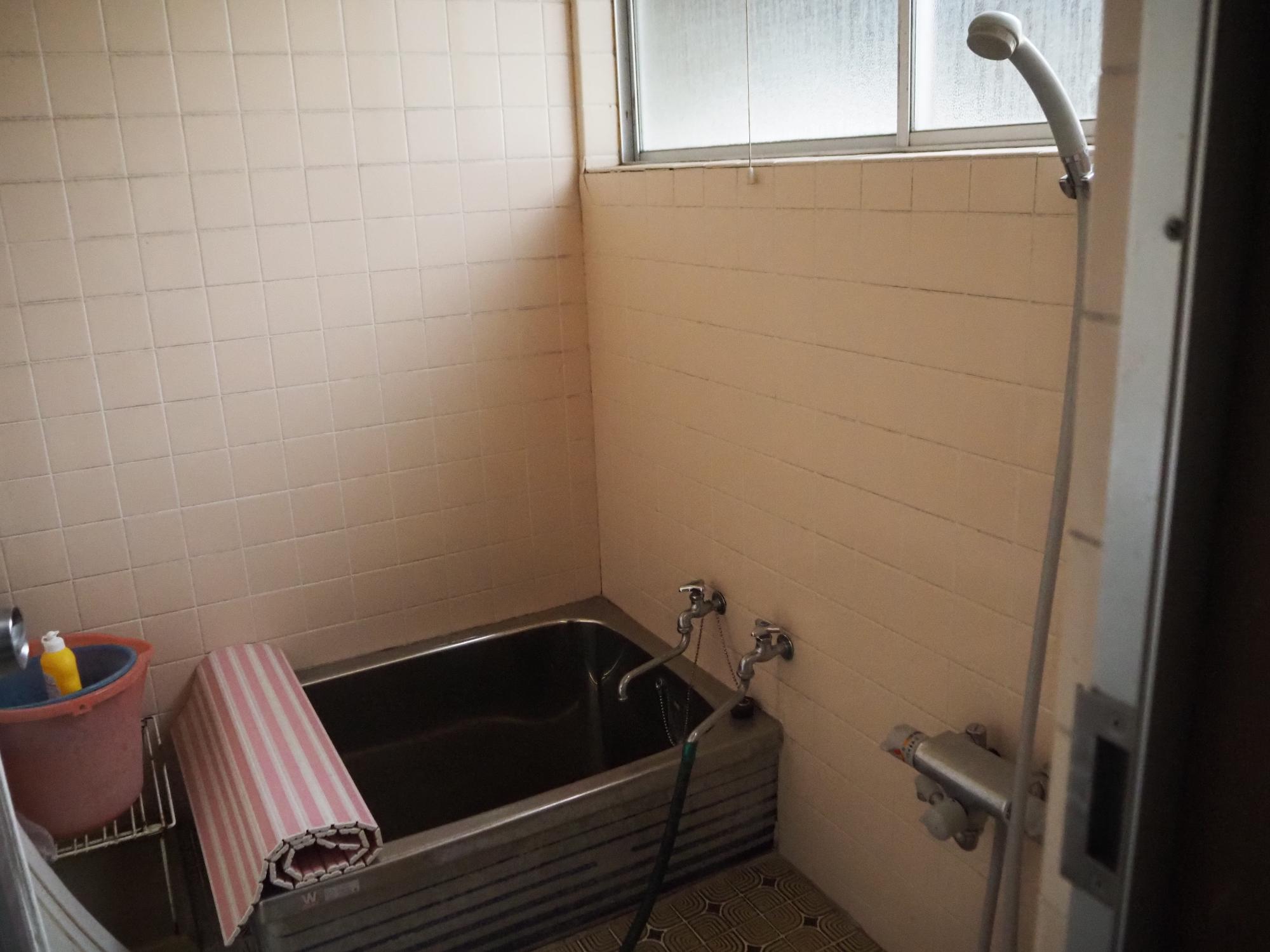 ピンクのタイル、ステンレスの浴槽、シャワー付きの風呂