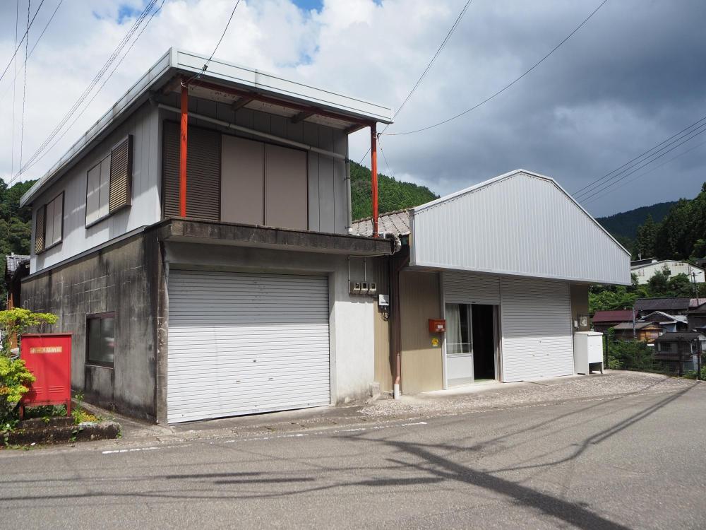 白い外観。店舗跡とシャッター付きの二階建て倉庫が並ぶ物件の写真。