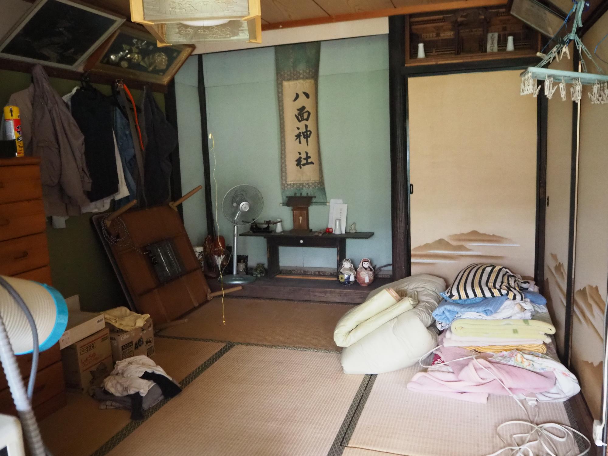床の間に掛け軸が有り、畳の上に布団が残っている和室の写真