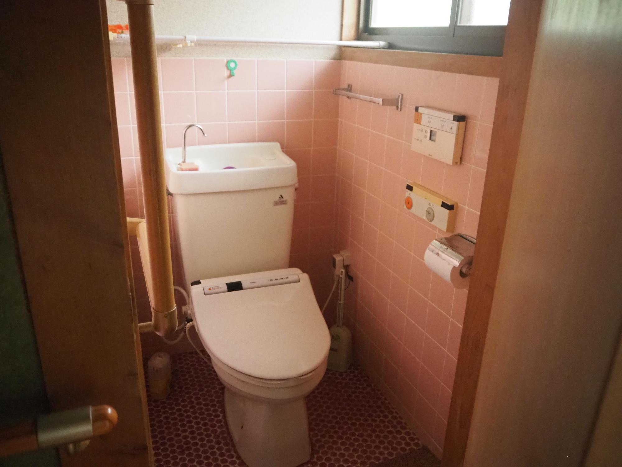 ピンクのタイルの壁に手すりが設置された洋式トイレの写真