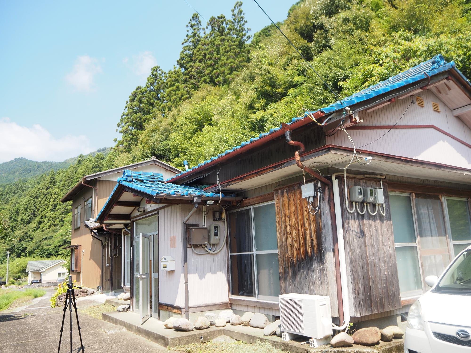 青い屋根の平屋建ての物件。奥には2階建ての納屋が見える写真