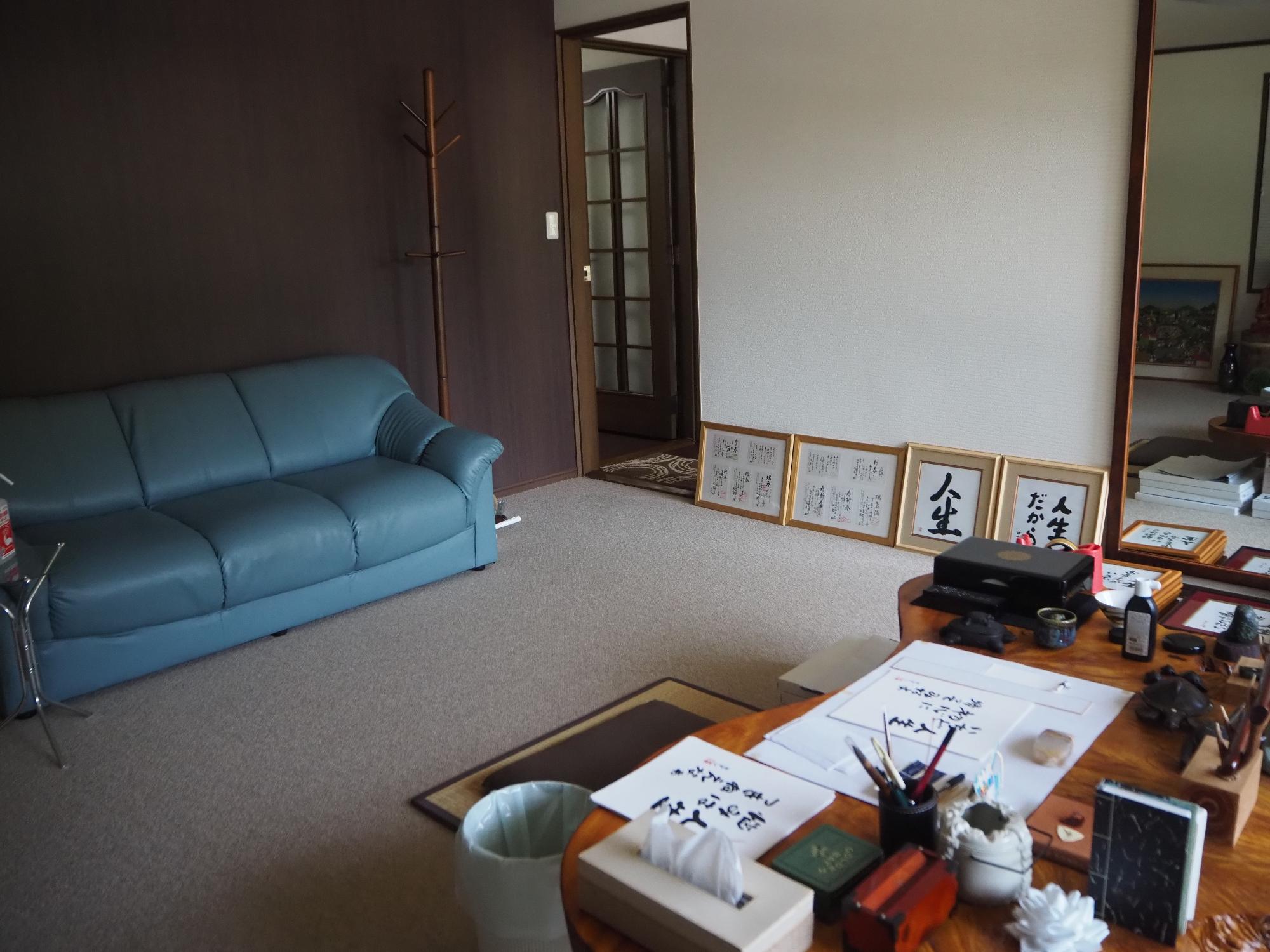 水色のソファと鏡、書道の作品が置かれた洋室