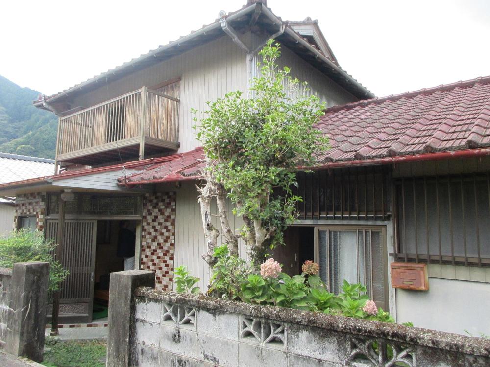 周りを木々に囲まれ、建物全体が白を基調とした外観、1階部分と2階部分にベランダが設置されている2階建て住宅の外観写真