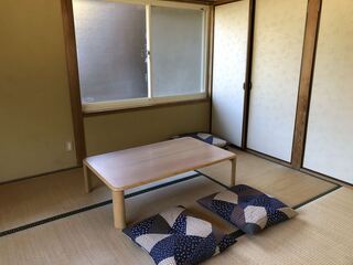 押し入れの横に窓があり、テーブルと座布団が2枚置かれた畳の部屋の写真