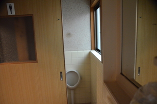 半開きの引き戸の奥に男性の小便器があるトイレの写真