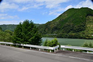 道路の先にダム湖や山並みが広がっている自然豊かな場所を撮った写真