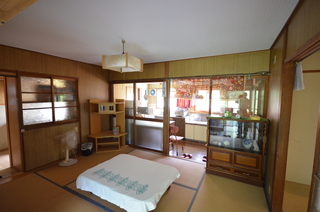 テーブル、扇風機、食器棚、テレビ台が置かれた和室の写真