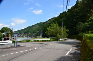 カーブを描いた道路の先に山並みや青空が広がっている自然豊かな場所を撮った写真