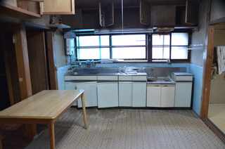 大きな窓から太陽の光が差しこみ、流し台の上の天井に収納棚が備え付けられているキッチンの写真