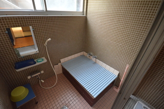 茶色のタイルの壁にシャワーヘッドが設置され、浴槽に水色の蓋が被せられた窓のある浴室の写真