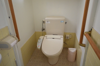白の壁紙に下半分ほどがタイル張り、両側の壁に手すりが設けられ様式のトイレが設置されているトイレの写真