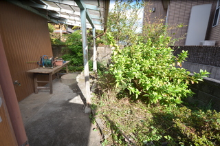庭に木が植えられ、軒下のテーブルに道具が置かれた玄関先の写真