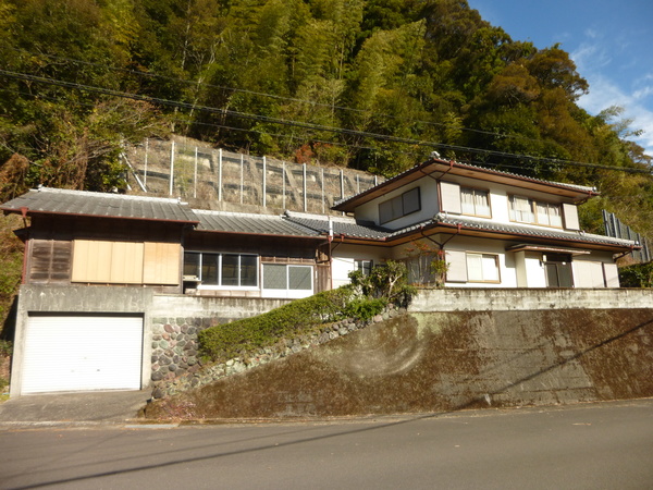 木々を背景に茶色の外壁で木造平屋の外観写真