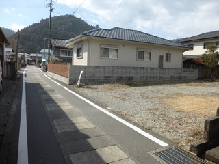 ブロック塀で仕切られ、道路沿いの右側にある空地の写真