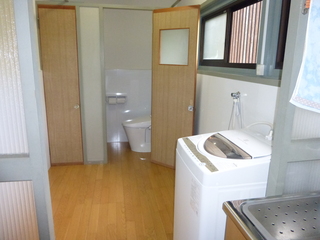 奥に洋式トイレ、右側に洗濯機のある室内写真