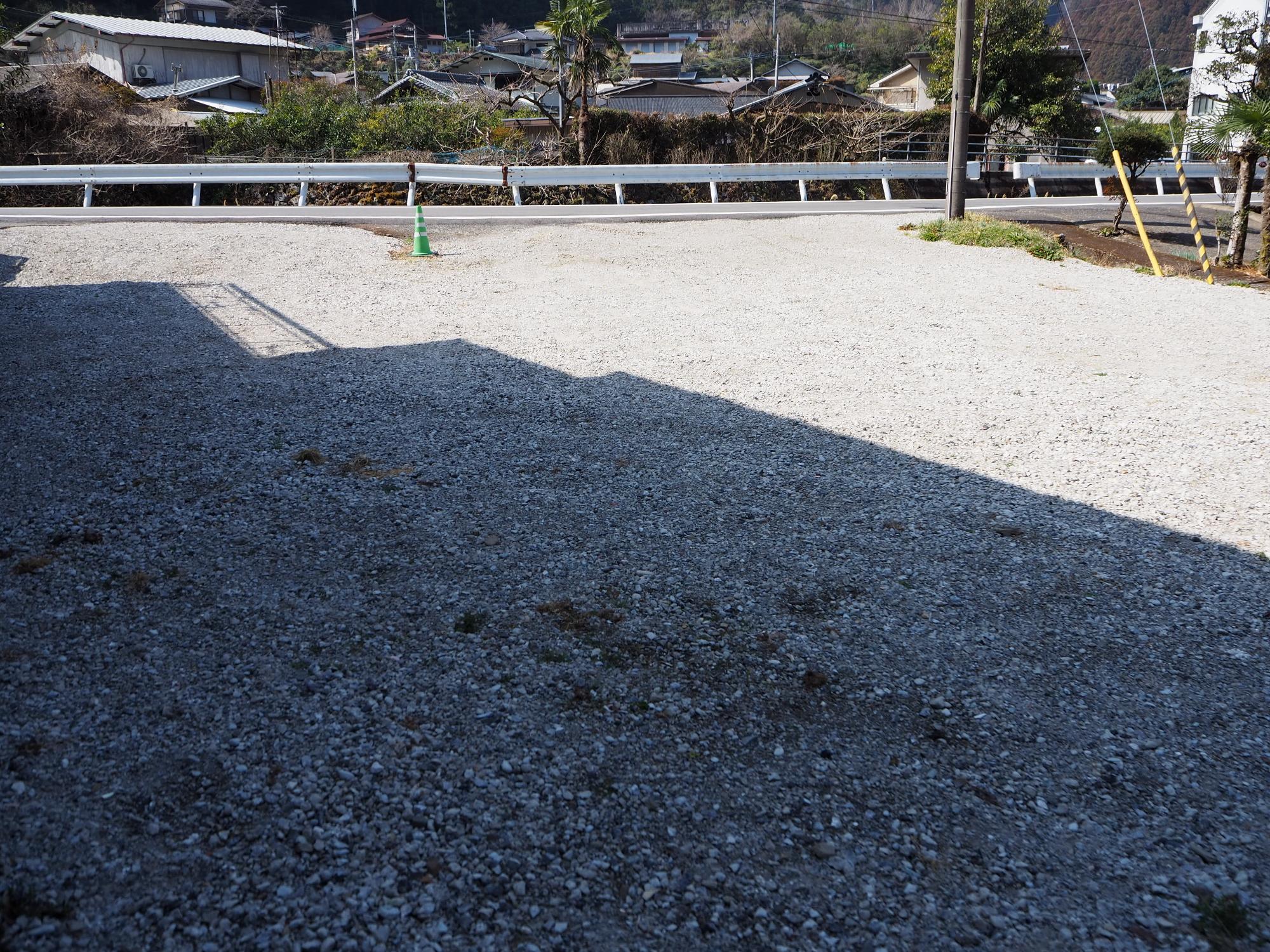 奥にガードレールがある道路沿いに砂利が敷かれた空地のある写真