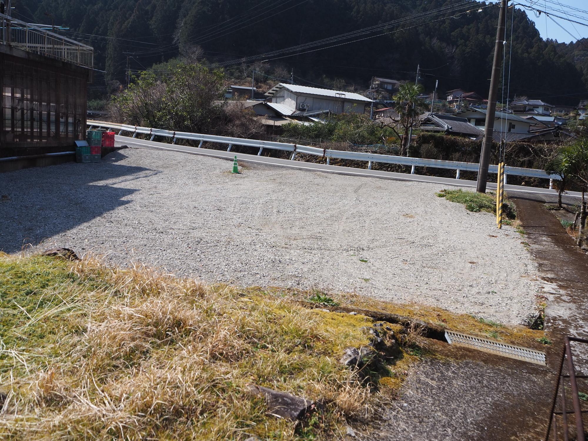 道路の奥には家が建ち並び、道路の手前に広々とした空地のある写真