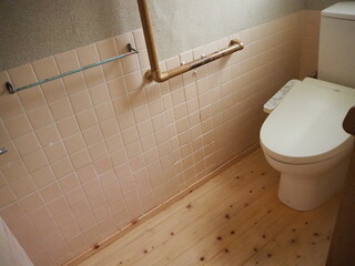 ピンクのタイルの壁に手すりやタオル掛けが設置された洋式トイレの写真