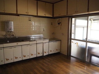 右側に窓があり、流し台の上の天井に収納棚が設置された台所の写真