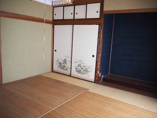 青い壁の床の間、左側に押入があり畳にシートが敷かれた和室の写真