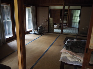 左側に窓があり、椅子や布団が置かれた二間続きの和室の写真