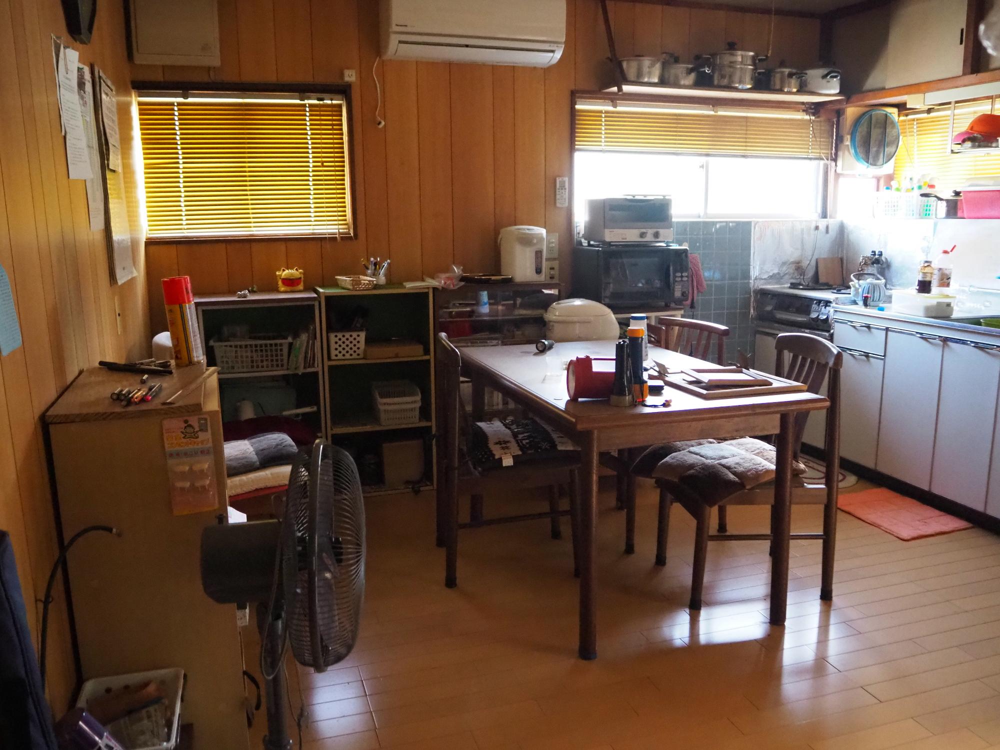 流し台が設置されており、テーブルと椅子があり電子レンジ、オーブントースター、炊飯器などが置かれている台所の写真