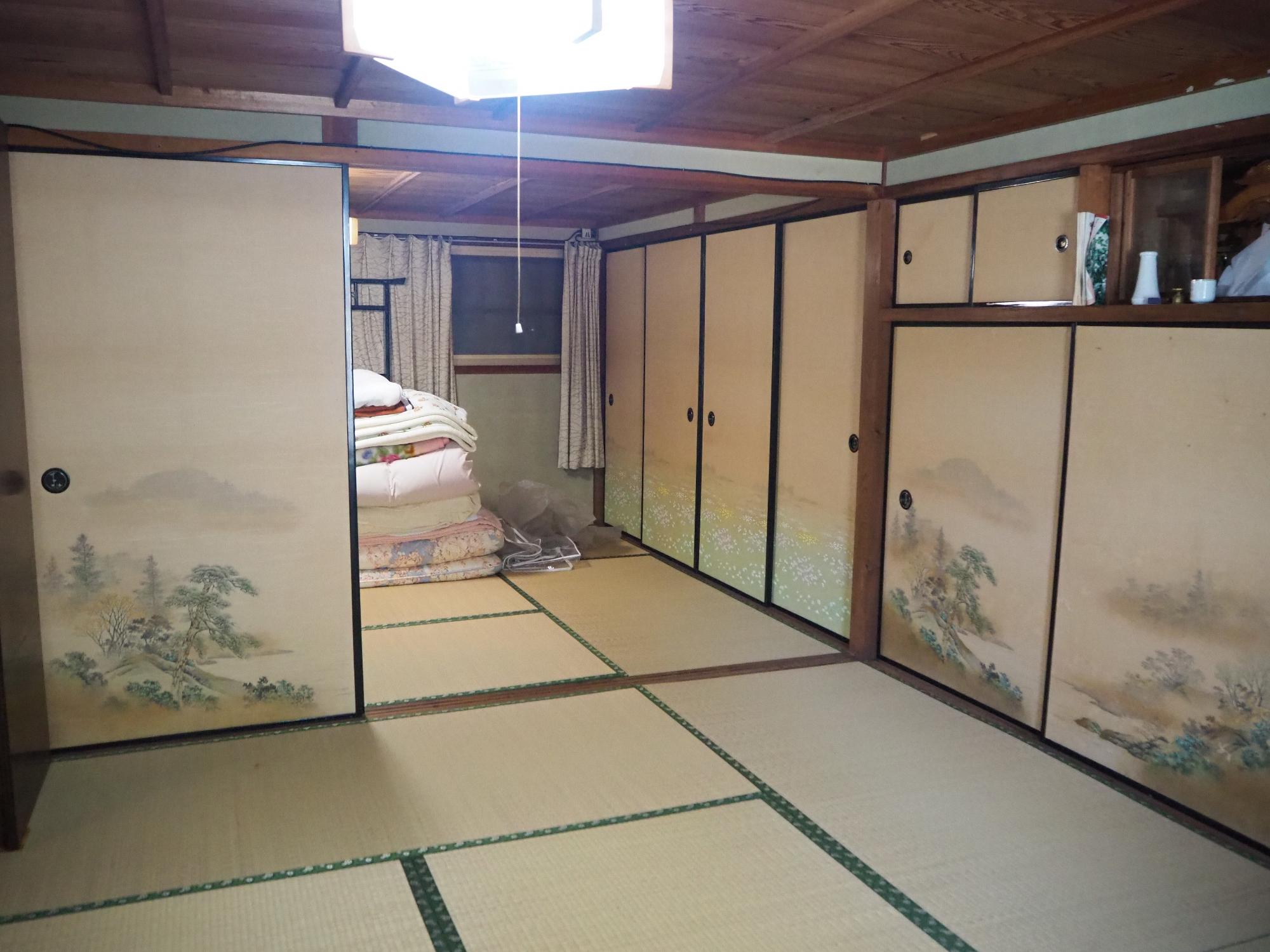 奥の和室には畳んだ布団が積まれた二間続きの和室の写真