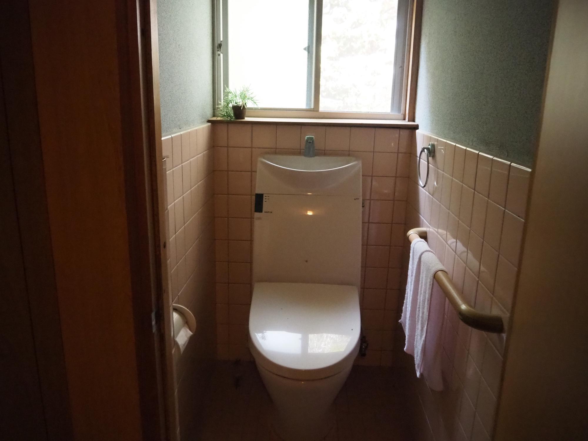 ピンクのタイルの壁に手すりが設置された洋式トイレの写真