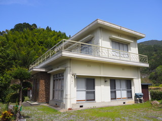白を基調とした木造2階建てで、2階にはベランダのある建物の外観写真